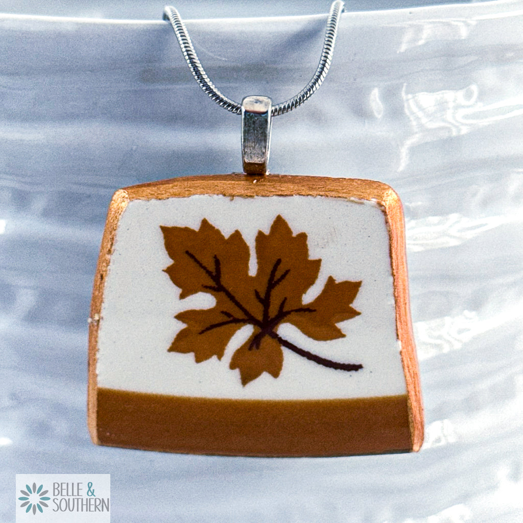 Square pendant with brown leaf design on a white background, attached to a chain.
