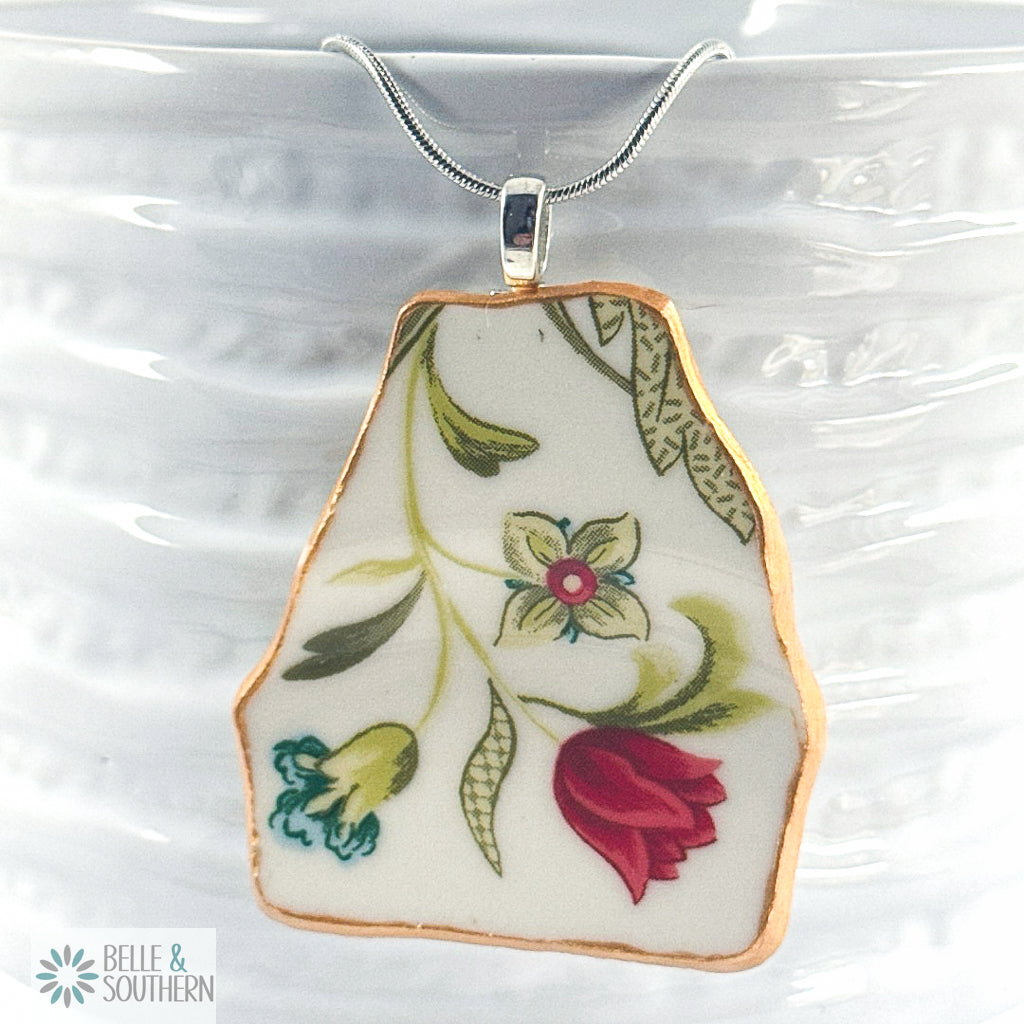 Red, teal and green floral print china on rhodium plated snake chain on a ceramic bowl.