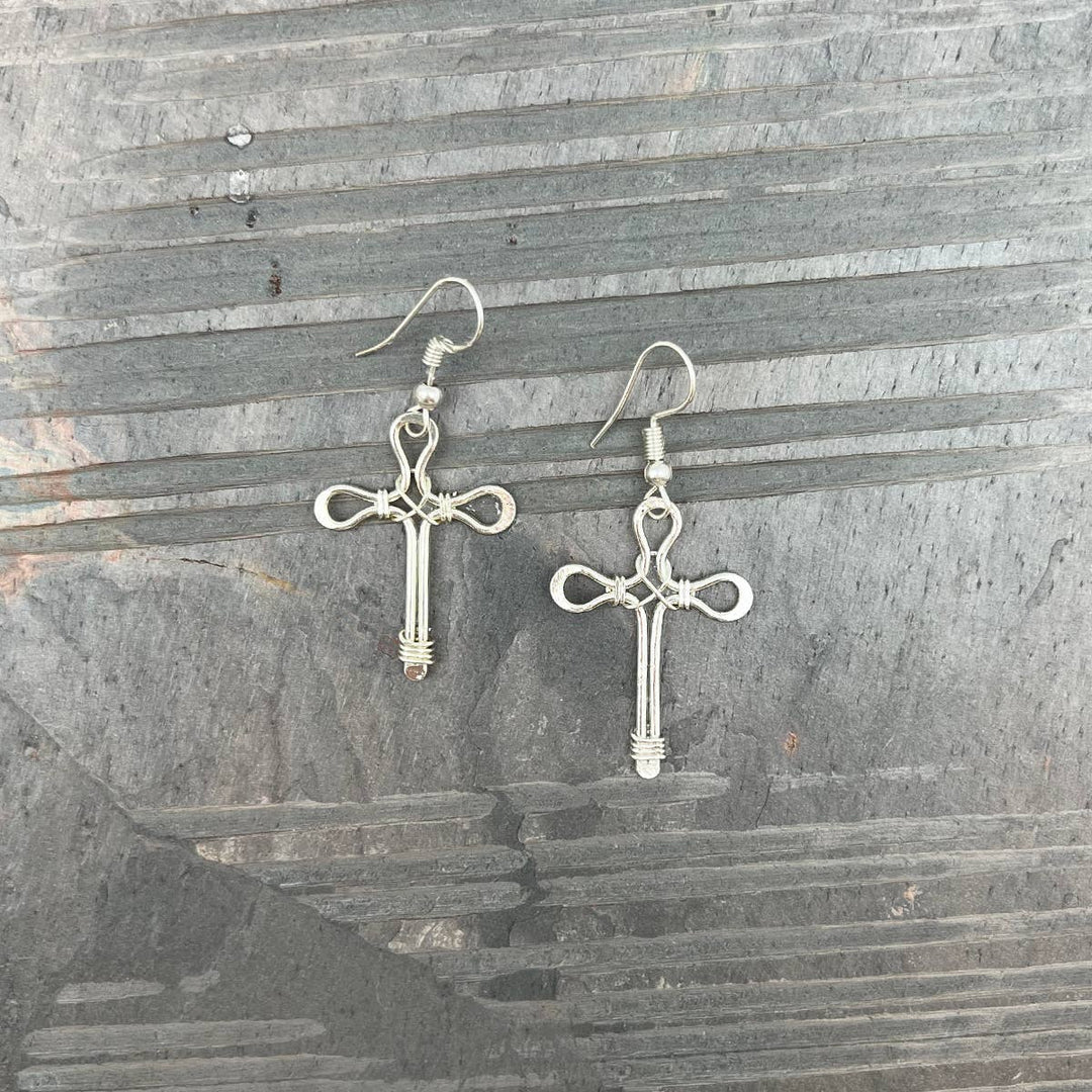 Silver-plated wire cross earrings with small hoop ear wires, displayed on a textured surface.