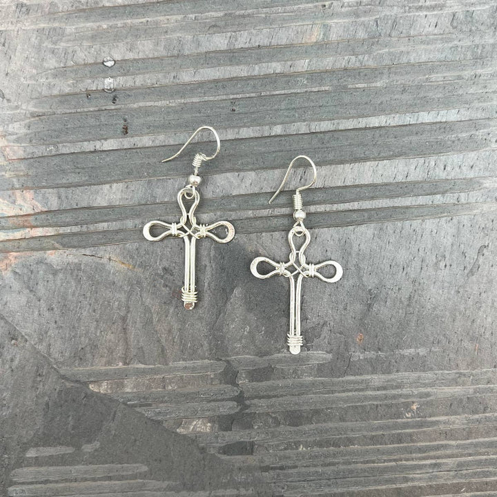 Silver-plated wire cross earrings with small hoop ear wires, displayed on a textured surface.