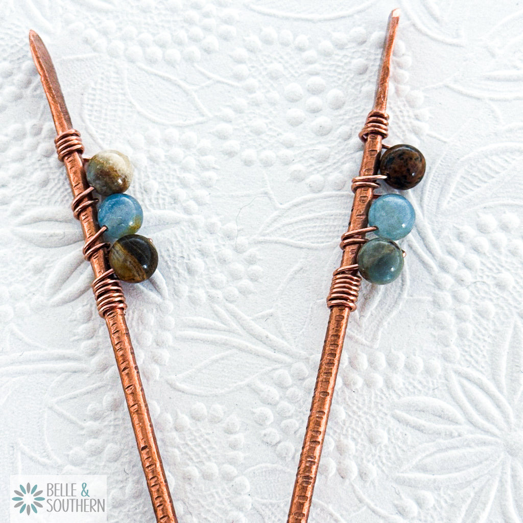 Pair of Aquatine Calcite Copper Hair Sticks Close Up n Floral background
