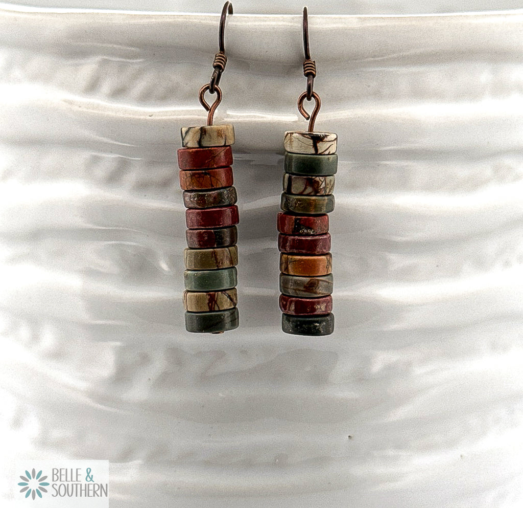 Stacked brown, green, tan, and rust color Red Creek Jasper Dangle Earrings on Niobium Ear wires displayed on a white ceramic vase.
