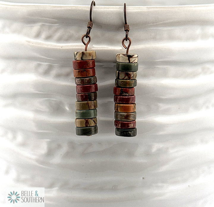 Stacked brown, green, tan, and rust color Red Creek Jasper Dangle Earrings on Niobium Ear wires displayed on a white ceramic vase.
