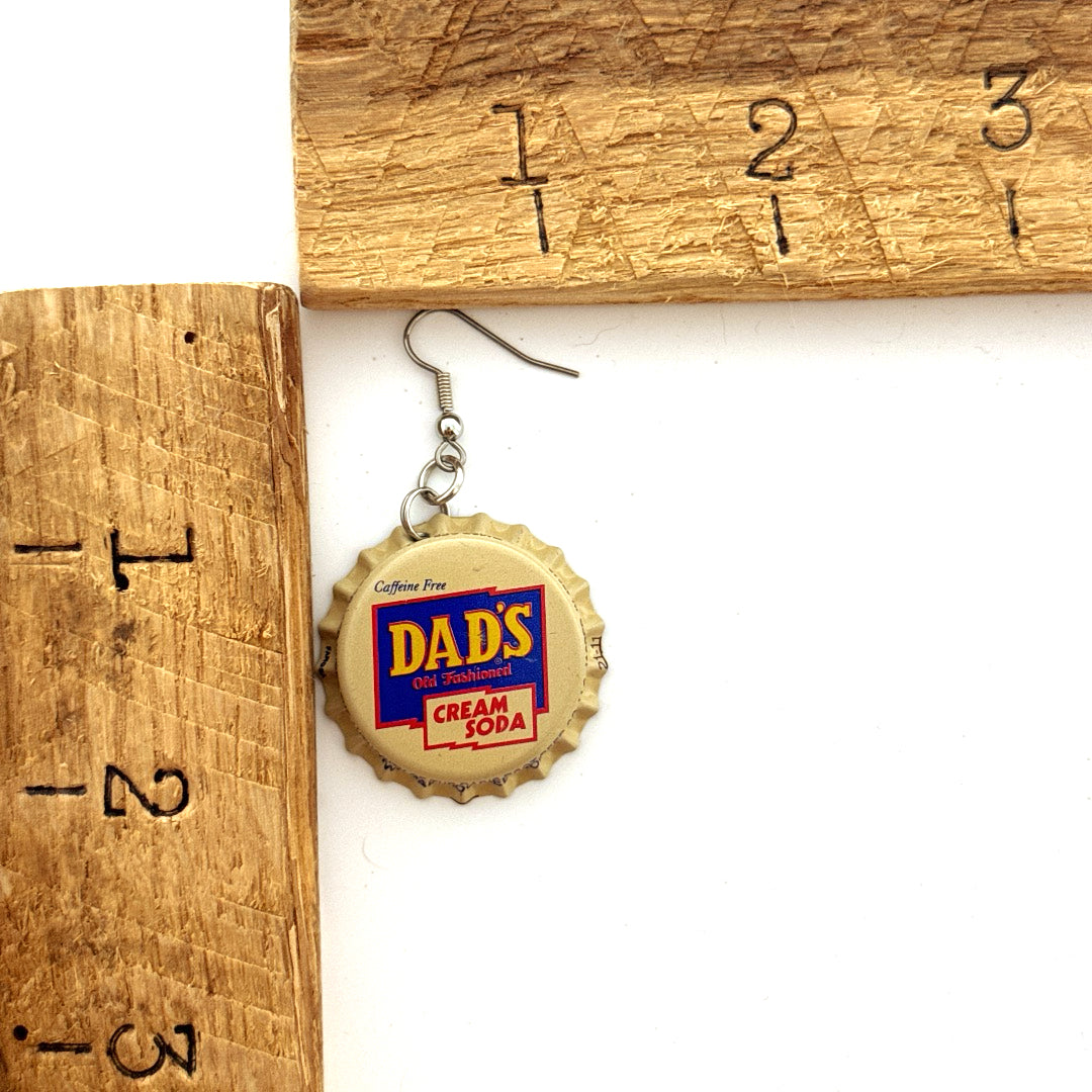 Cream and Blue Dad's Cream Soda Bottle Cap on Stainless Steel Ear Wires next to ruler