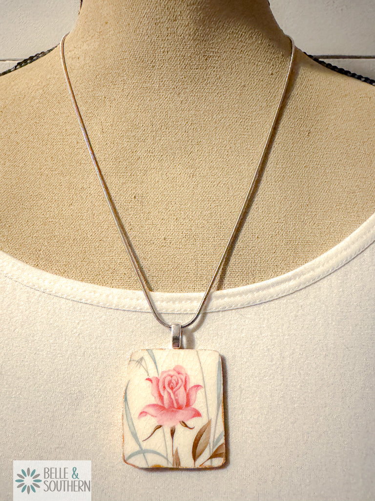 Necklace with a pendant featuring a pink rose design on a mannequin bust.