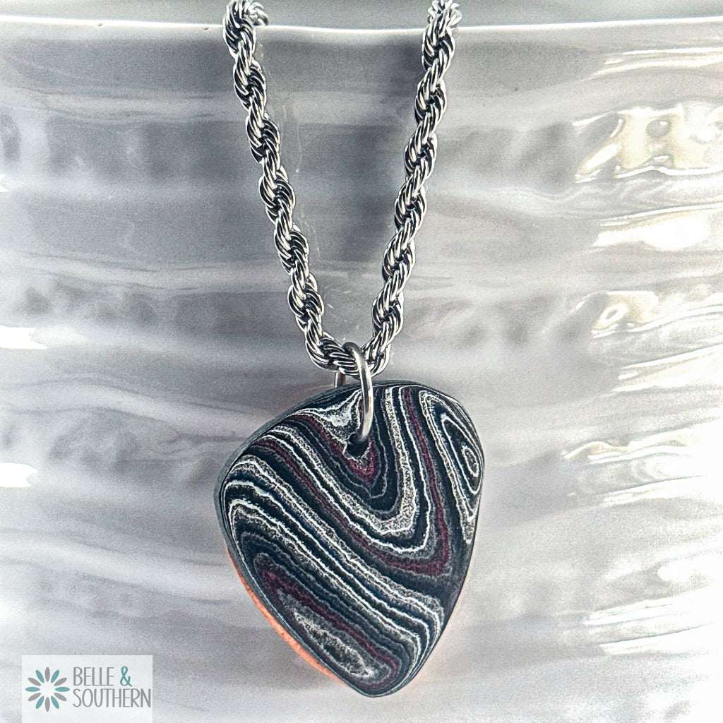 Necklace with a multicolor Fordite with copper Guitar pick pendant on white vase, featuring the brand 'Belle & Southern'.
