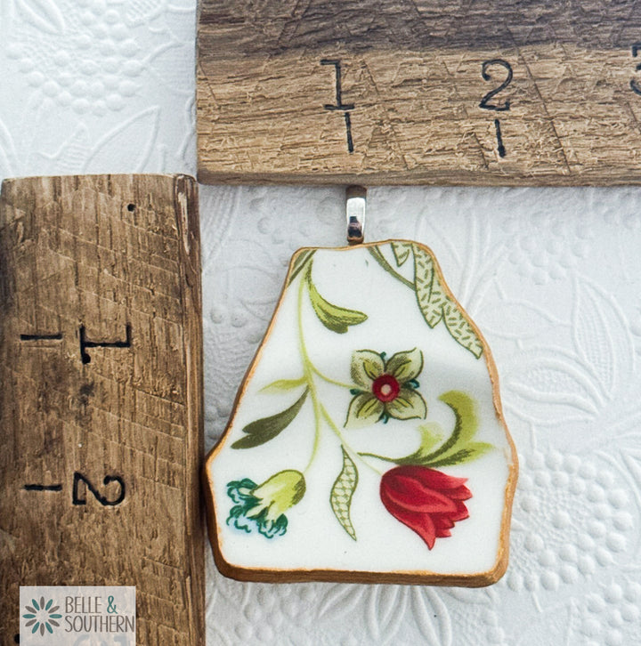 Decorative ceramic pendant with floral design on a white background with wooden rulers for scale.