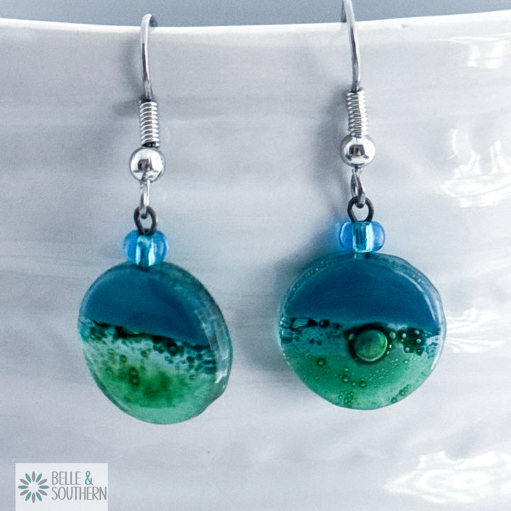 Pair of blue and green fusion glass earrings on a white vase with 'Belle & Southern' branding.