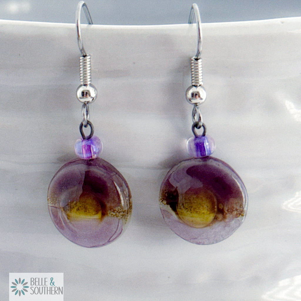 Purple and gold round fusion glass earrings on a white vase with 'Belle & Southern' branding.