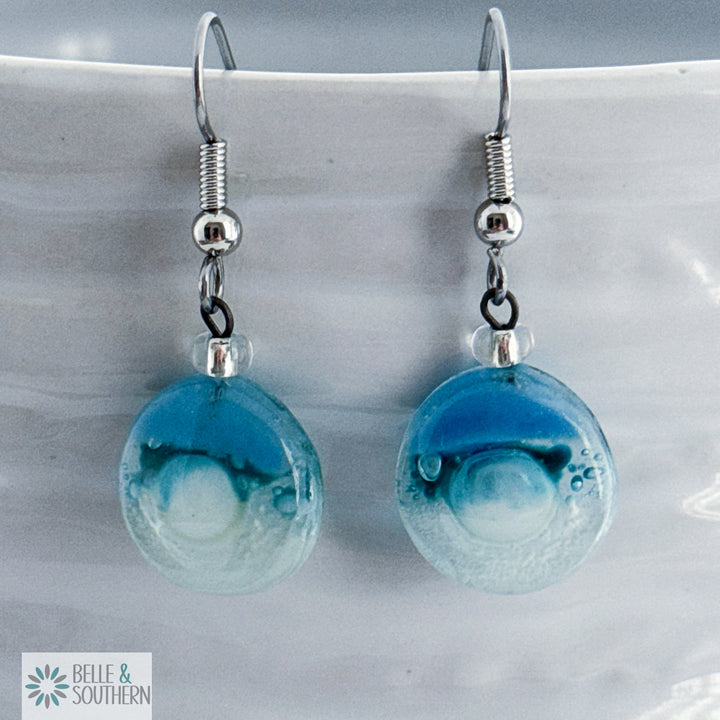 Blue and Clear fused circle glassed earrings on stainless steel ear wires resting on a white vase