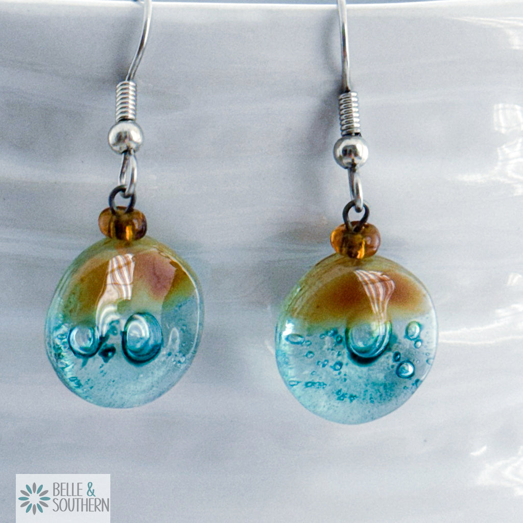 Amber and light blue circular fusion glass earrings with a stainless steel ear wire  on a white vase, branded 'Belle & Southern'.