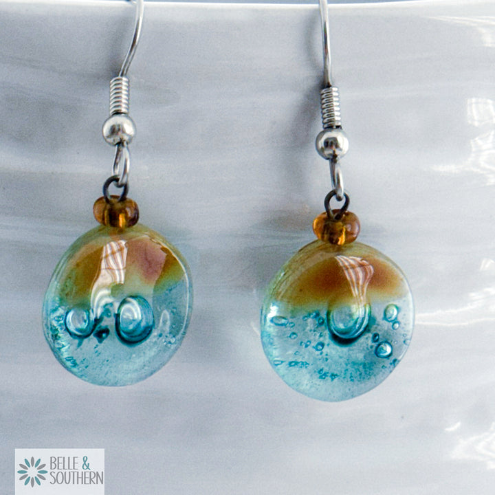 Amber and light blue circular fusion glass earrings with a stainless steel ear wire  on a white vase, branded 'Belle & Southern'.