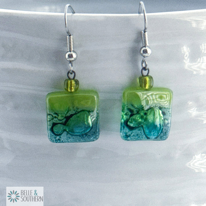 Light green and light blue fused glass square earrings on stainless steel ear wires on a porcelain vase
