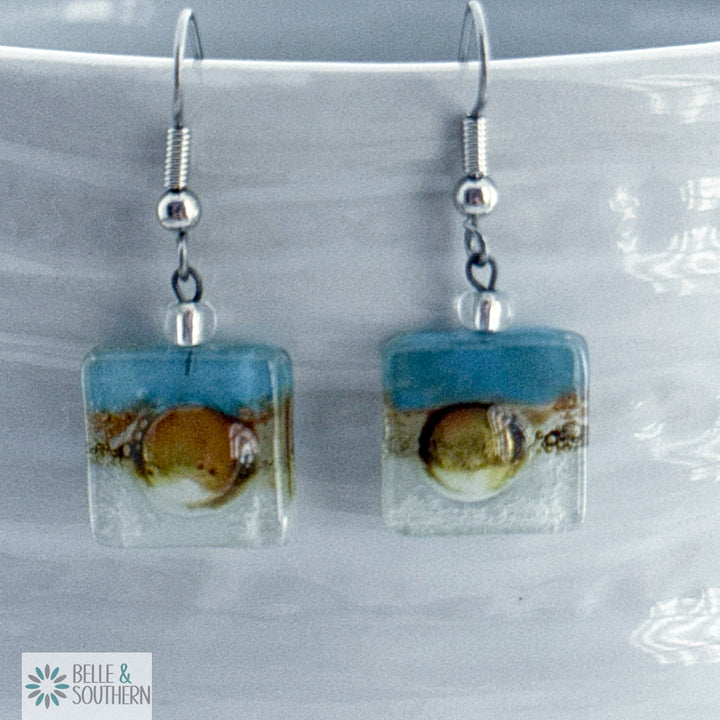 Light blue, gold and clear fused glass square earrings on stainless steel ear wires on a porcelain vase
