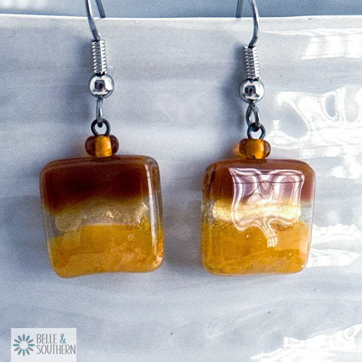 Brown and gold fused glass square earrings on stainless steel ear wires on a porcelain vase
