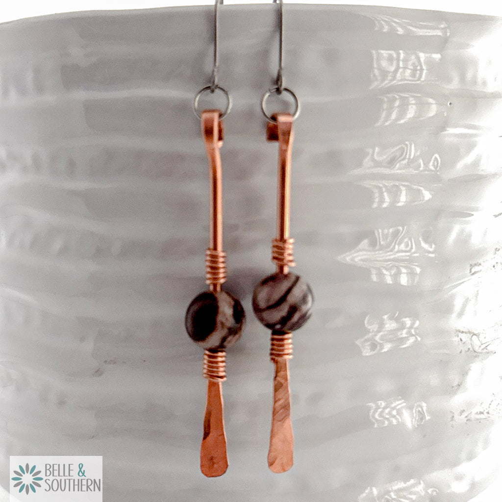 Zebra Jasper gemstone on copper dangle earrings resting on a white vase