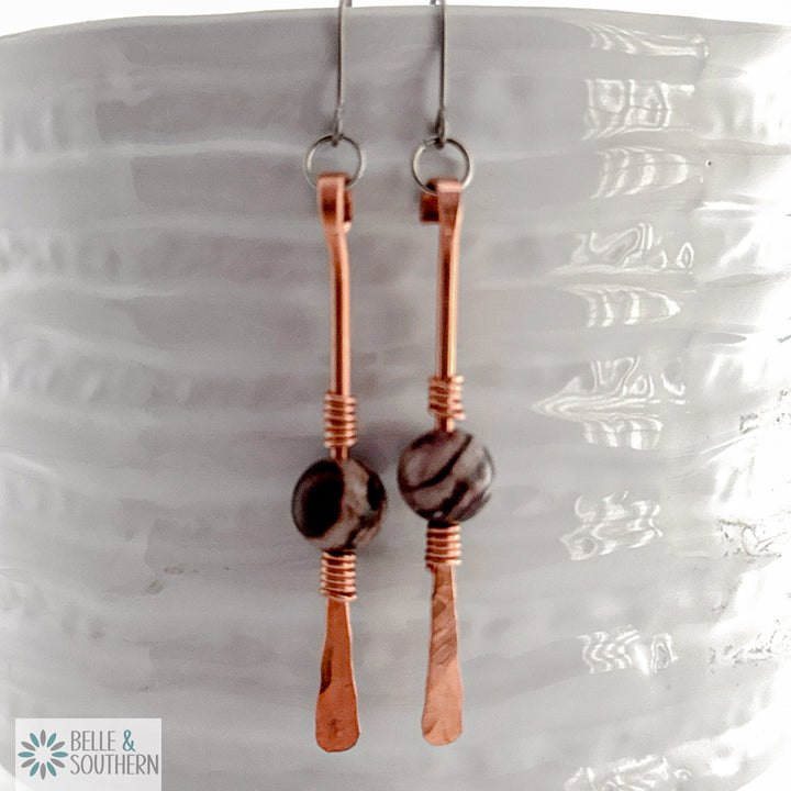 Zebra Jasper gemstone on copper dangle earrings resting on a white vase