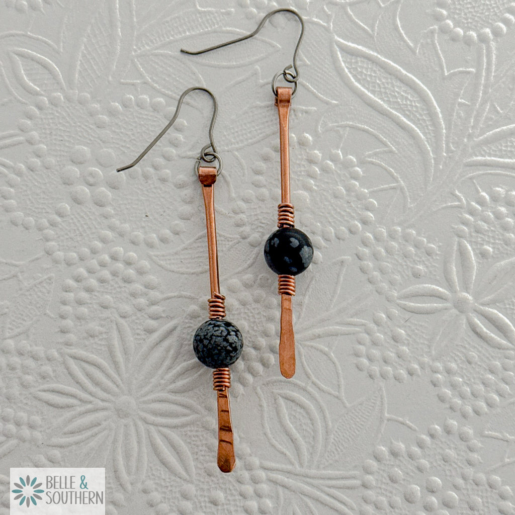 Copper and snowflake obsidian gemstone dangle earrings on a white embossed background