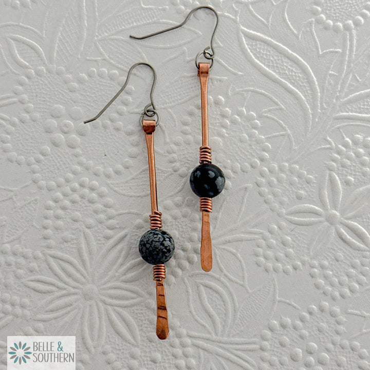 Copper and snowflake obsidian gemstone dangle earrings on a white embossed background