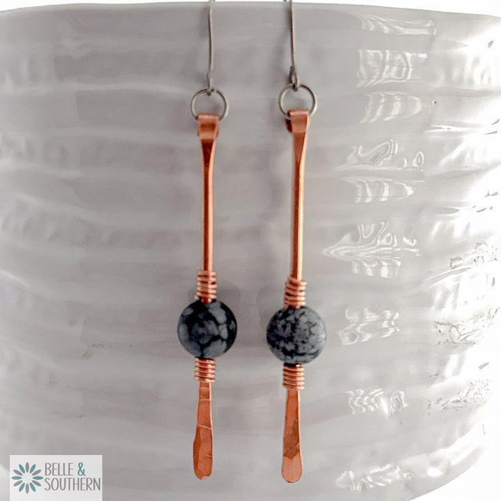 Copper dangle with snowflake obsidian gemstone dangle on titanium ear wires resting on a white vase