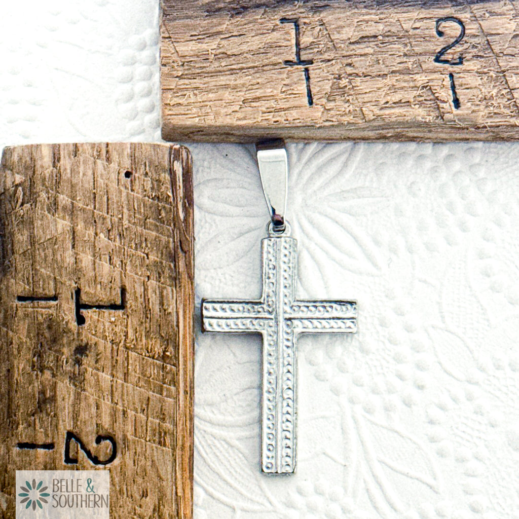 Silver cross pendant by rulers background with 'Belle & Southern' branding.
