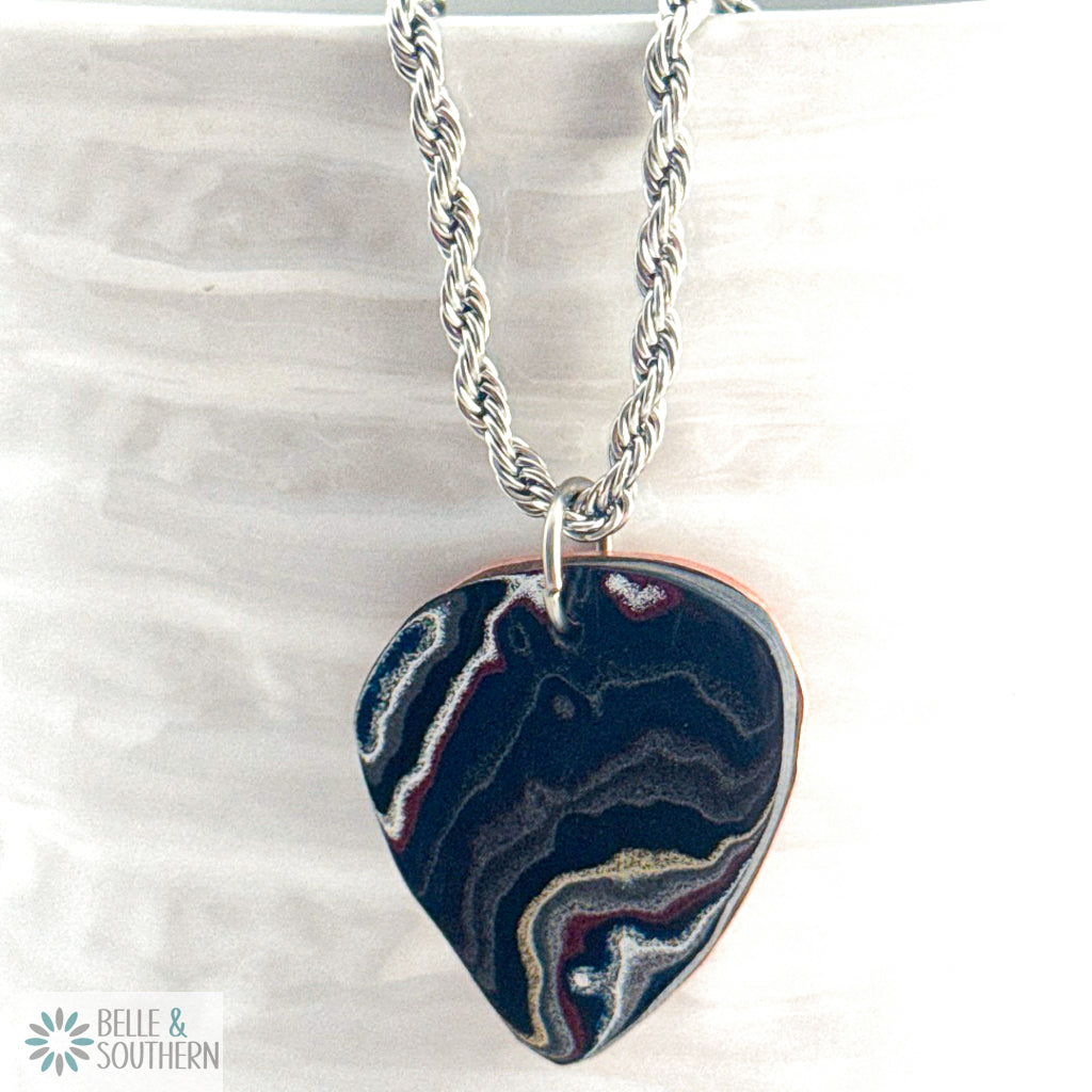 Guitar Pick Fordite with wavy ribbons of maroon, gold-tan, soft grey, and white swirl through the surface sitting on a copper backplate hanging on Stainless Steel Rope Chain
