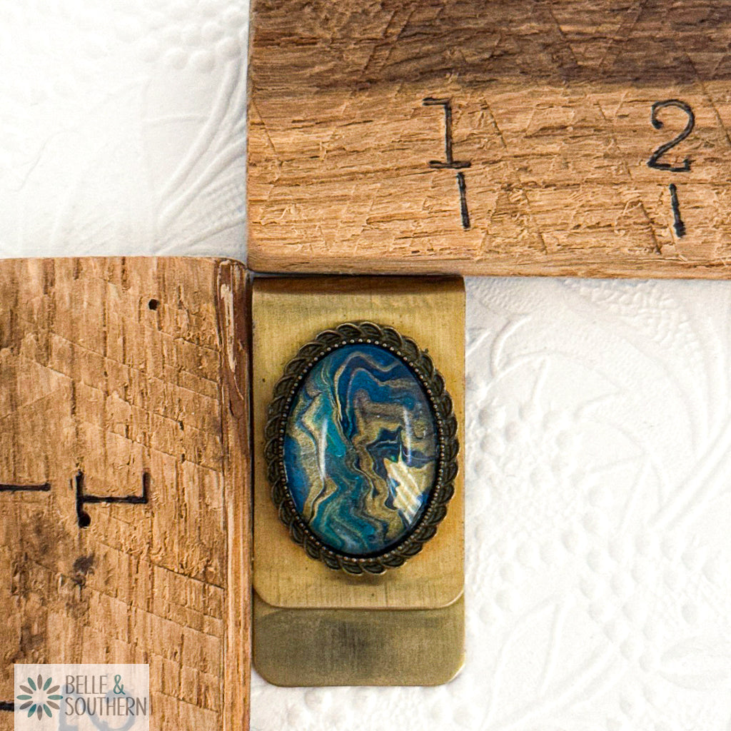 Gold Stainless Steel Money Clip with Blue, Teal, and Gold marbled stone looking paint with decorative border by ruler, branded 'Belle & Southern'.
