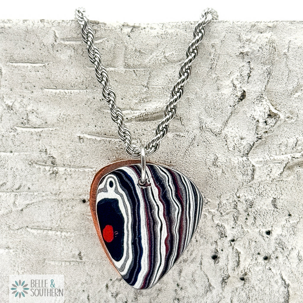 Necklace with a Fordite Guitar Pick shape pendant on a textured surface, branded 'Belle & Southern'.