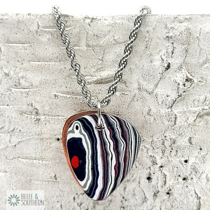 Necklace with a Fordite Guitar Pick shape pendant on a textured surface, branded 'Belle & Southern'.