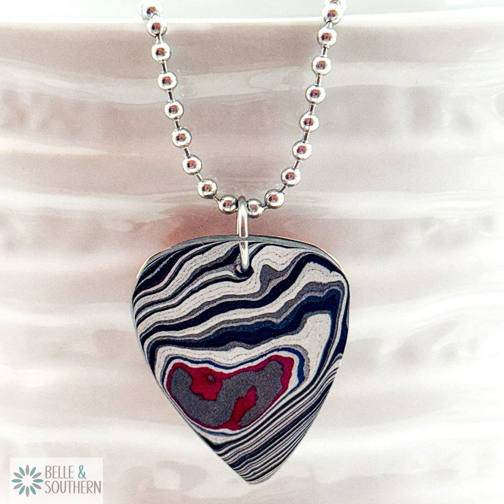 Motor City Pick Crimson Core Pattern Fordite in a guitar pick shape resting on a copper backplate on a stainless steel ball chain
