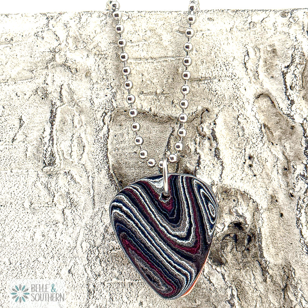 Fordite Guitar Pick Necklace on a bead chain up against a stone surface
