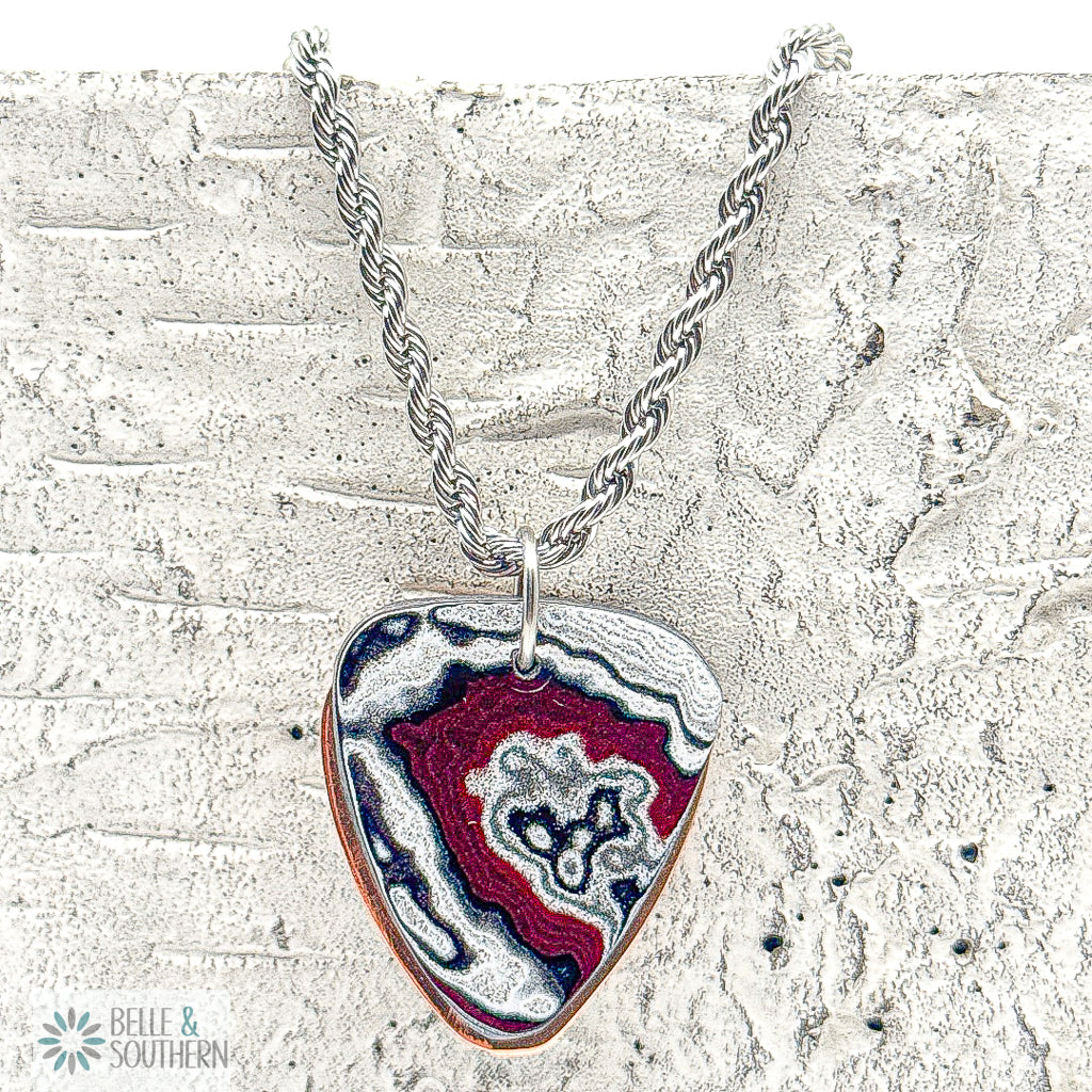 Fordite Guitar PIck Shaped Pendant on Rope Chain Necklace on a stone backdrop