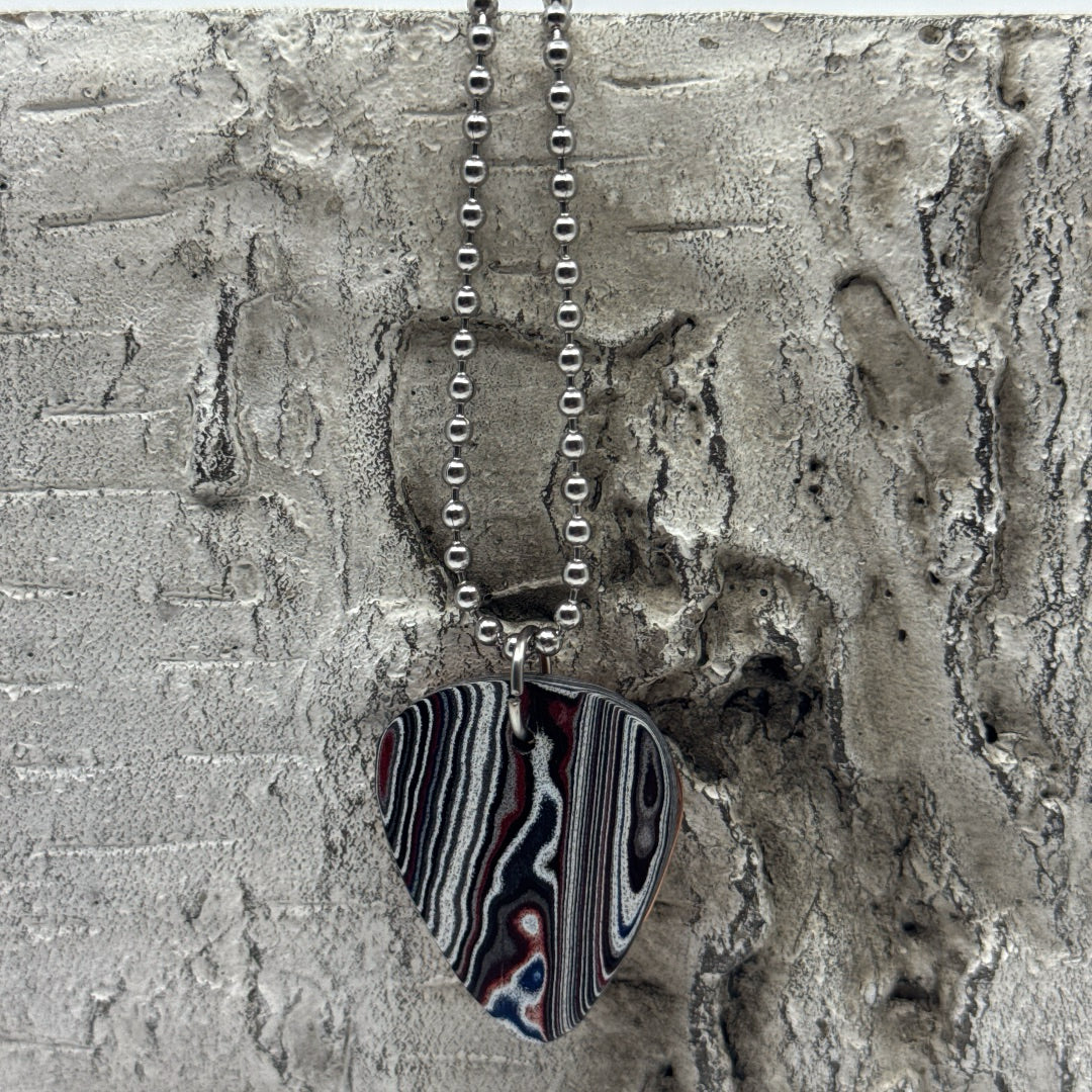 Necklace with a guitar pick-shaped pendant on a textured surface with bead chain