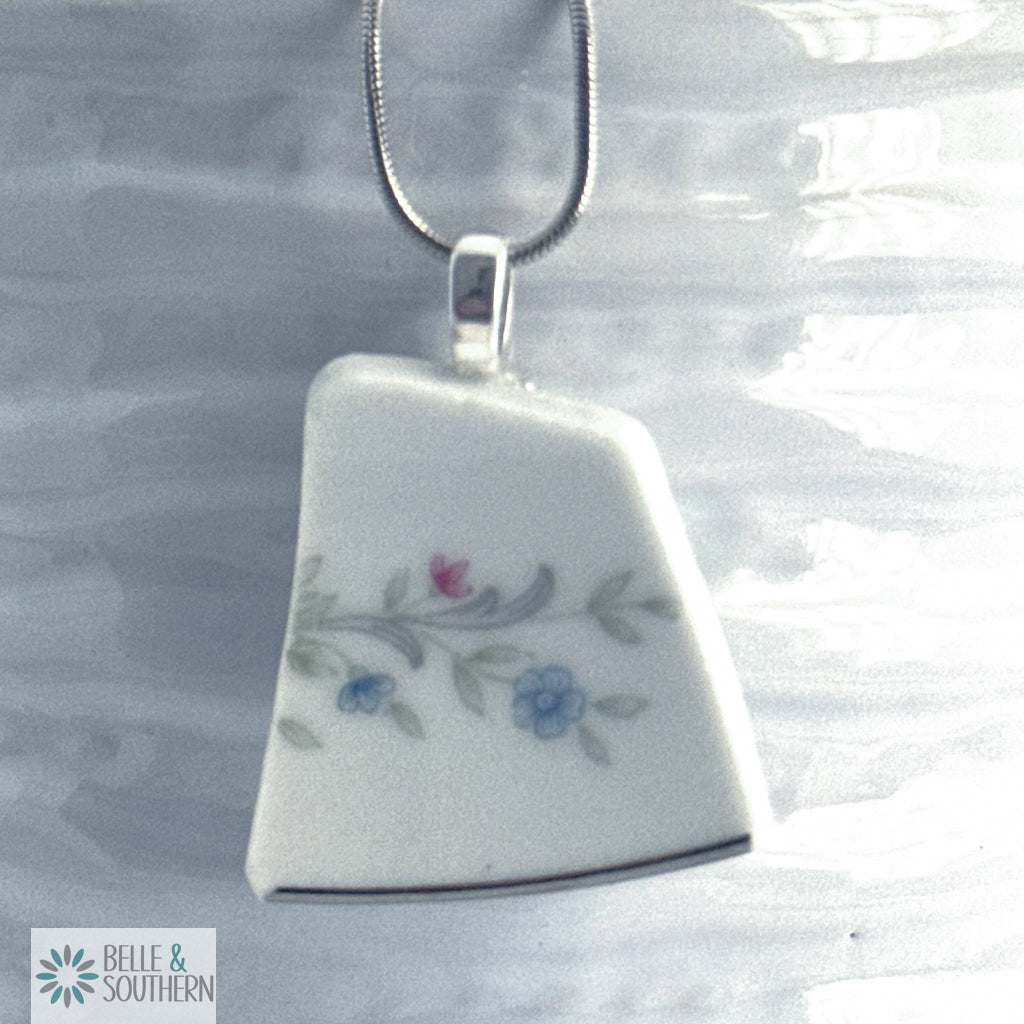 White ceramic pendant with floral design on a silver chain against a gray background