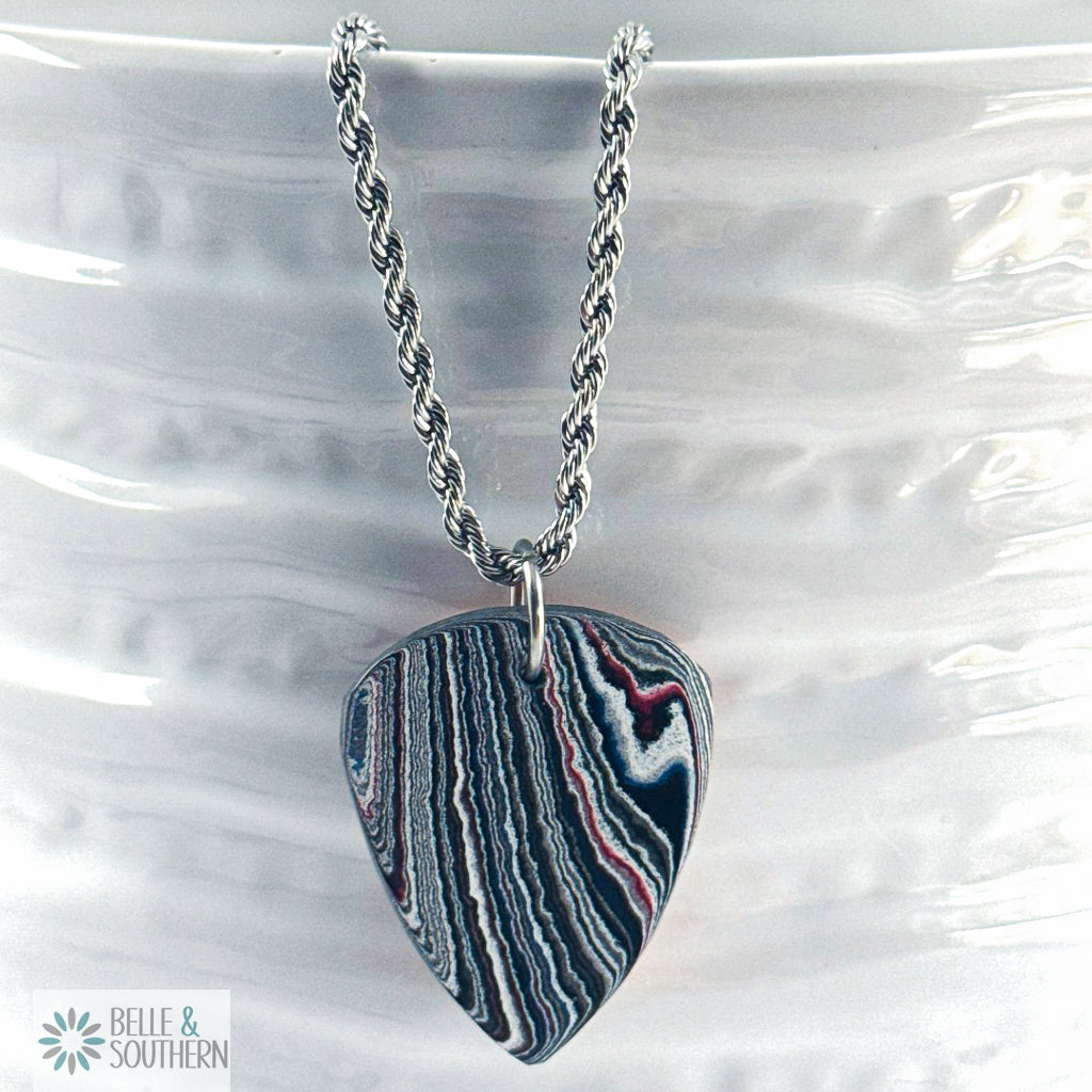 Necklace with a multi colored Fordite with copper guitar pick pendant on a white vase, featuring the brand 'Belle & Southern'.