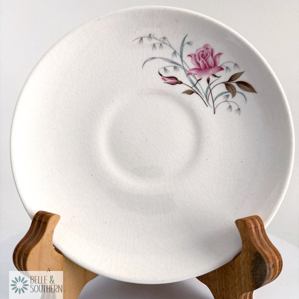 White ceramic plate with floral design on a wooden stand against a white background