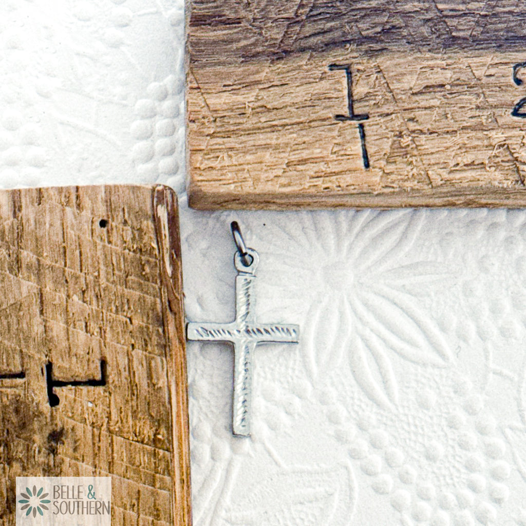 Silver cross pendant on a textured white surface by wooden rulers in the background.