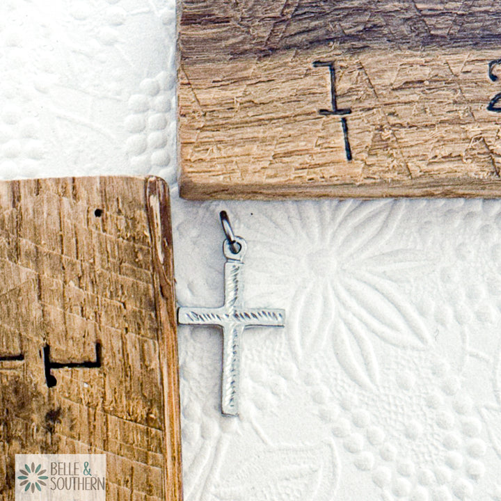 Silver cross pendant on a textured white surface by wooden rulers in the background.