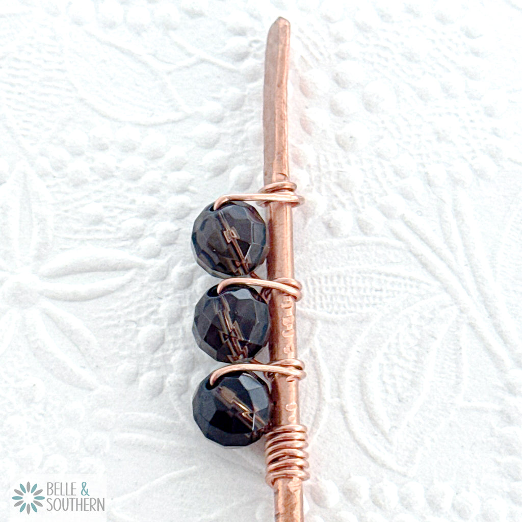 Close-up of faceted smoky quartz gemstone beads wrapped on a textured copper hair stick shown for reference 