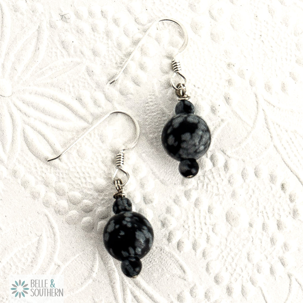 Black snowflake obsidian beads on argentium silver ear wires on a white textured background