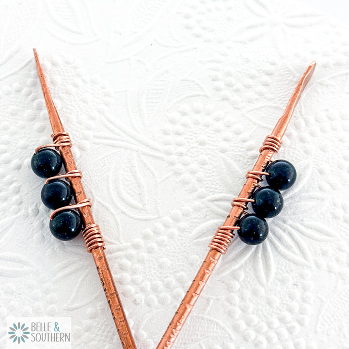 Sparkling Green Goldstong wrapped on textured copper hair  stick resting on a floral pattern backgroun
