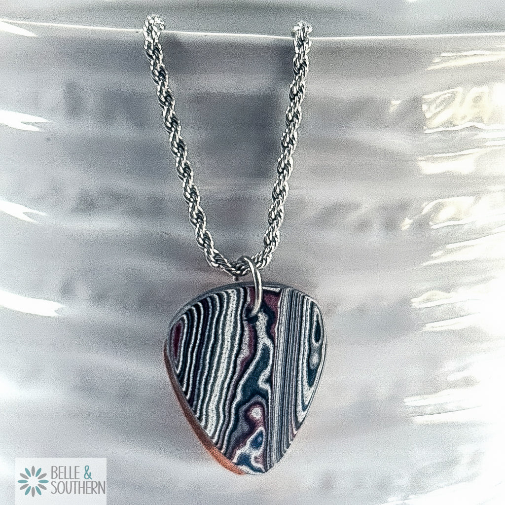 Multiple colored Fordite Guitar Pendant Necklace on white vase featuring the brand 'Belle & Southern'.