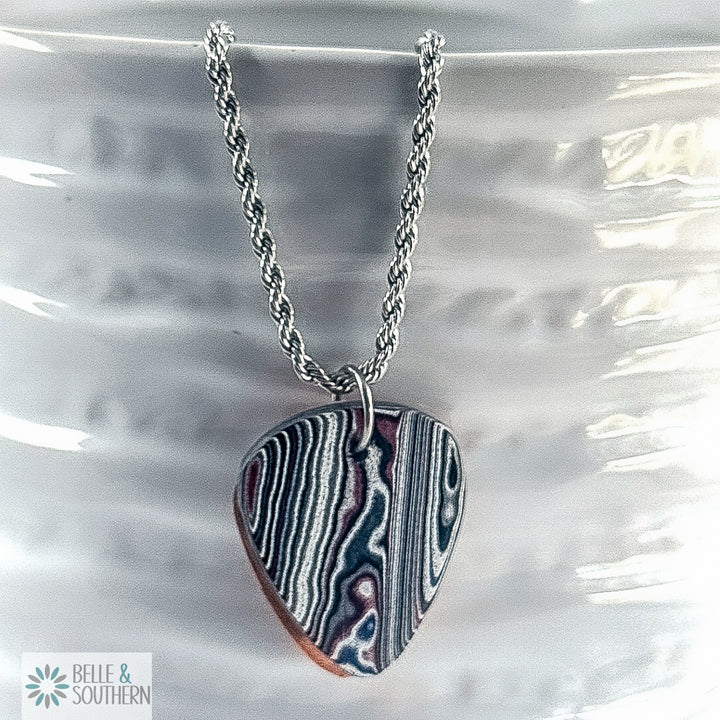 Multiple colored Fordite Guitar Pendant Necklace on white vase featuring the brand 'Belle & Southern'.