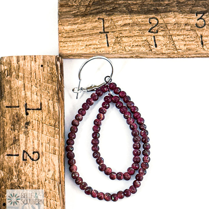 Cranberry beaded earrings on a white surface with a wooden ruler for scale.