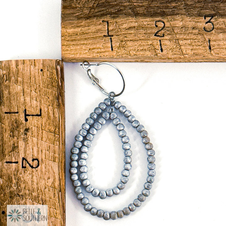 Silver beaded earrings on a white surface with a wooden ruler for scale.
