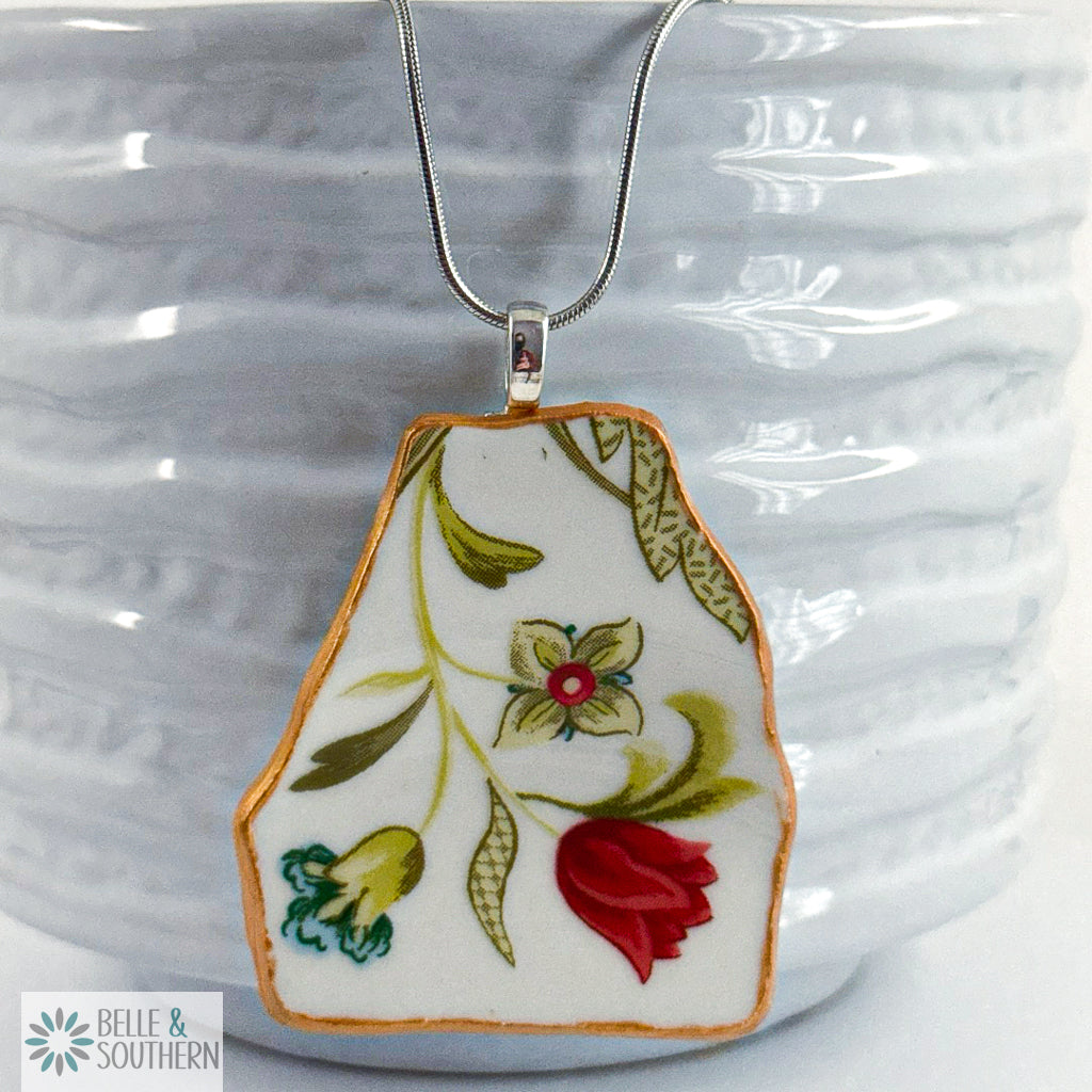 Handcrafted porcelain fragment necklace featuring a tropical red flower with teal and sage accents.