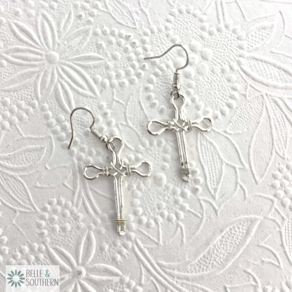 Silver cross earrings on a textured white background