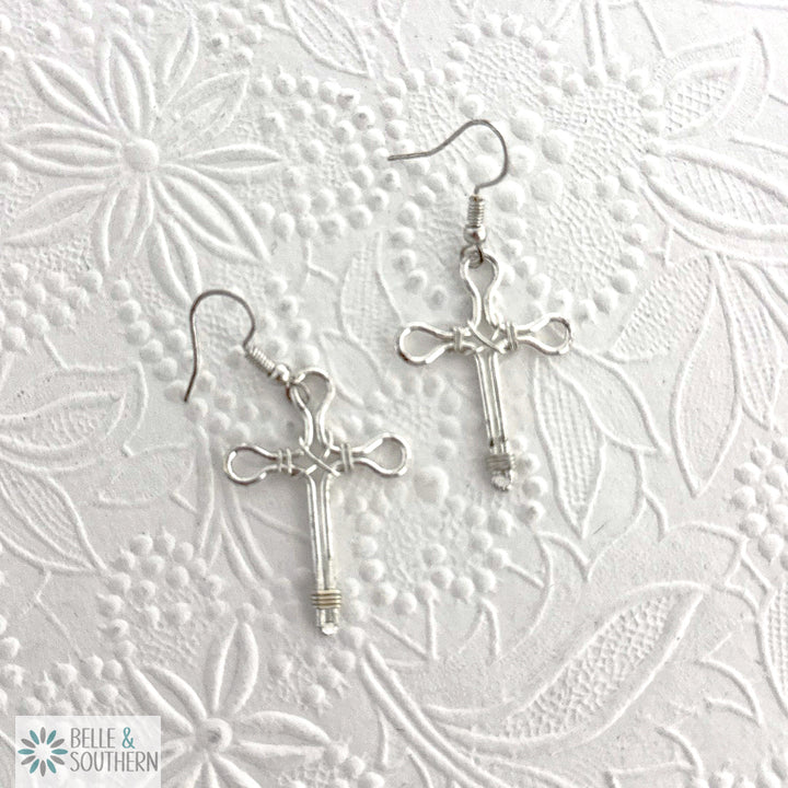 Silver cross earrings on a textured white background
